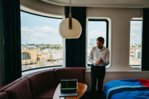 Man in room with laptop overlooking cityscape.