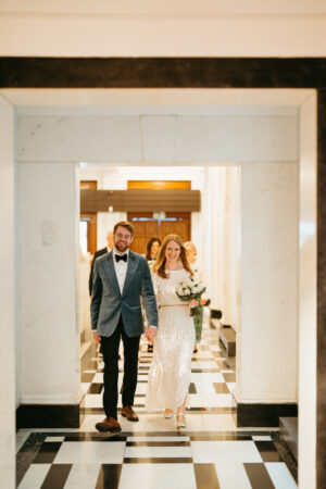 Couple walking hand in hand in marble hallway.