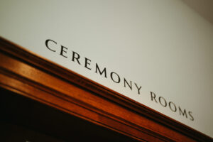 Sign reading "Ceremony Rooms" on wooden door frame.