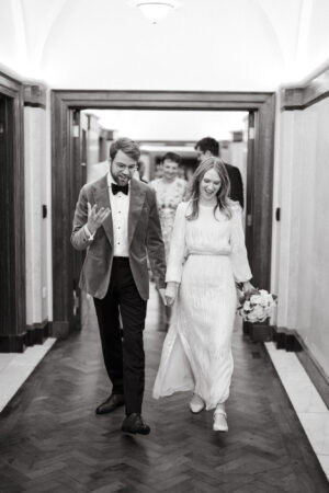 Couple walking and smiling in hallway, wedding attire.