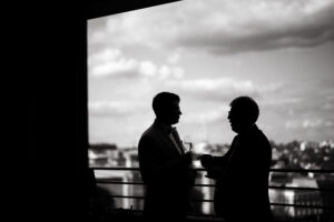 Two men conversing with drinks in silhouette.