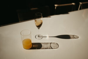 Champagne and orange juice glasses casting shadows on table.