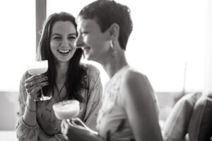 Two women laughing with cocktails in black and white.