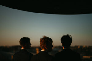 Three men in suits overlooking city skyline at dusk.