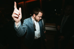 Man in blue suit gesturing at party.