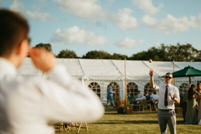 Gentleman playing catch at outdoor wedding event.