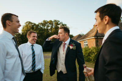 Groomsmen laughing together at outdoor wedding event.