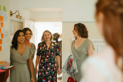 Women smiling indoors, joyful gathering, elegant dresses.