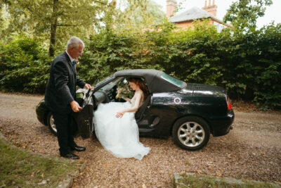 Bride entering car with assistance on wedding day.
