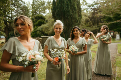 Bridesmaids with bouquets walking in garden.