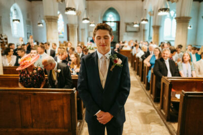 Groom waiting in church aisle with guests