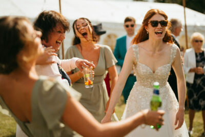 Bride laughing with guests at sunny outdoor wedding.
