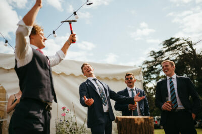 Men laughing during outdoor wedding reception game.