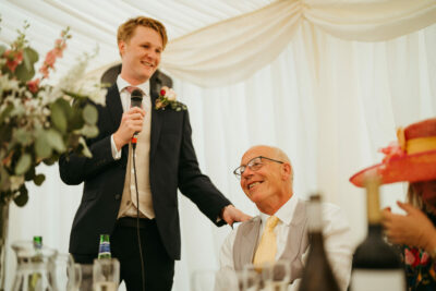 Wedding speech with smiling guests in marquee.