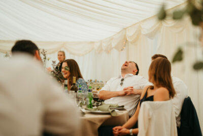 Guests laughing at wedding reception in tent.
