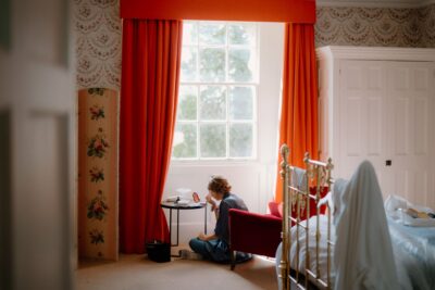 Person doing makeup in a room with orange curtains.
