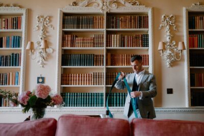 Man adjusting tie in elegant library setting.