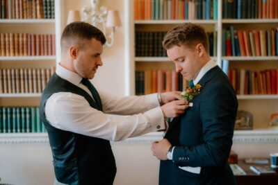 Groom getting boutonnière pinned on suit jacket.