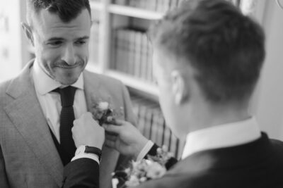 Groom being helped with boutonniere before wedding ceremony.