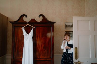 Woman on phone next to wardrobe with white dress.