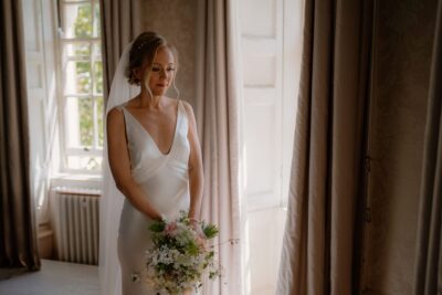 Bride holding bouquet by window in wedding dress