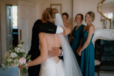 Bride embracing man at wedding, bridesmaids watching.
