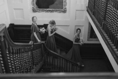 Bridesmaids ascending ornate staircase with bouquets.
