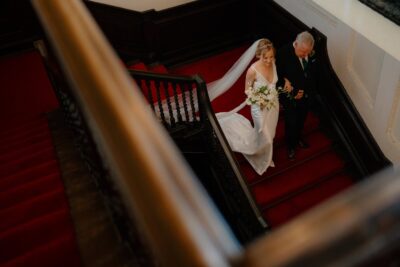Bride and groom ascending red-carpeted stairs.
