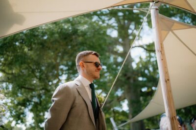 Man in suit at outdoor event with trees.