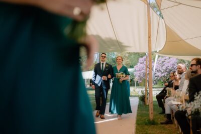Bridal couple walking down outdoor aisle, guests seated.
