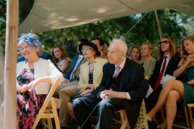 Guests sitting at outdoor event under canopy.