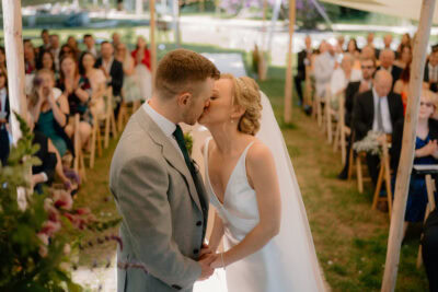 Bride and groom kissing at outdoor wedding ceremony.