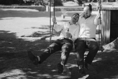 Two men laughing on a swing outdoors.