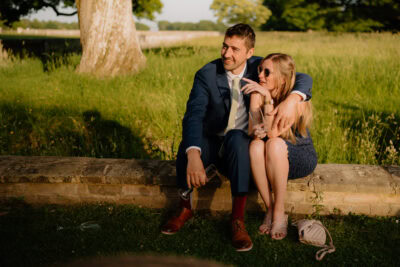 Couple sitting on a grassy stone wall, smiling.