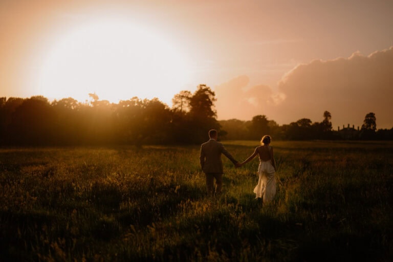 Couple holding hands at sunset in a field.