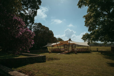 Event tent in serene parkland with flowering shrubs.
