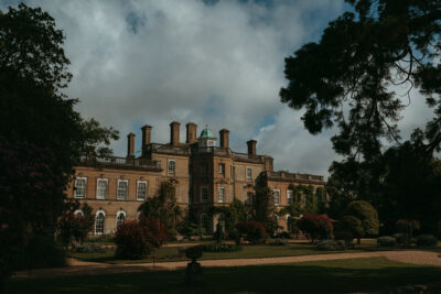 Historic manor house with gardens under cloudy sky.