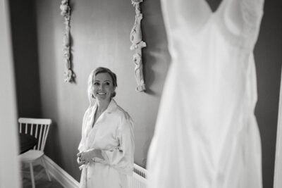 Bride in robe smiling beside wedding dress