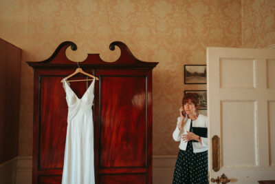 Woman on phone beside wedding dress in room.