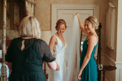 Bride trying on veil with friends' help.