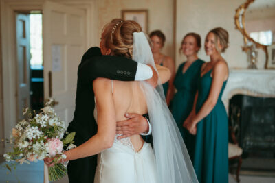 Bride hugging person at wedding, bridesmaids smiling.