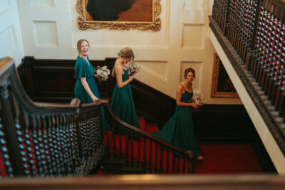 Bridesmaids in green dresses laughing on staircase.
