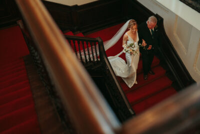 Bride and father descending staircase on wedding day.
