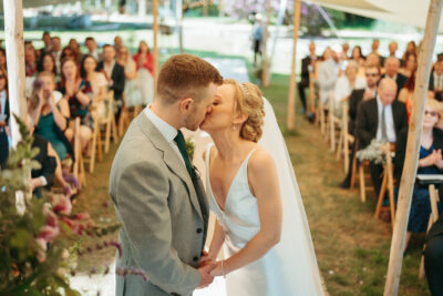 Bride and groom kissing at wedding ceremony with guests.