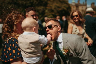 Wedding guest playing with baby outdoors in sunny weather.