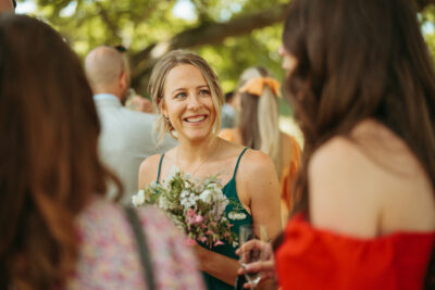 Woman smiling at wedding with bouquet and champagne.