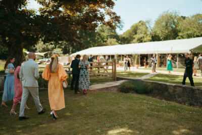Outdoor wedding reception with guests and marquee in background.