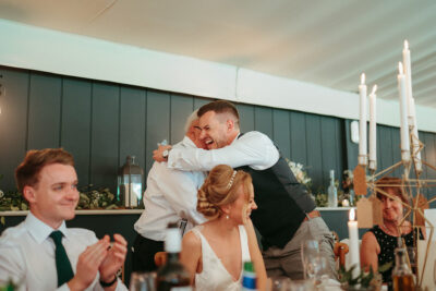 Joyful wedding embrace at reception table.