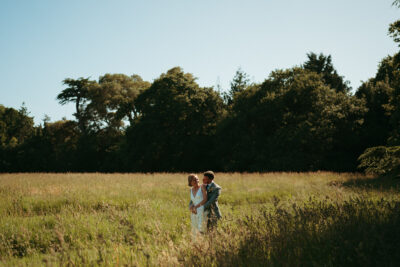 Couple embracing in sunlit meadow with trees.