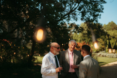 Three men chatting outdoors at sunset event.